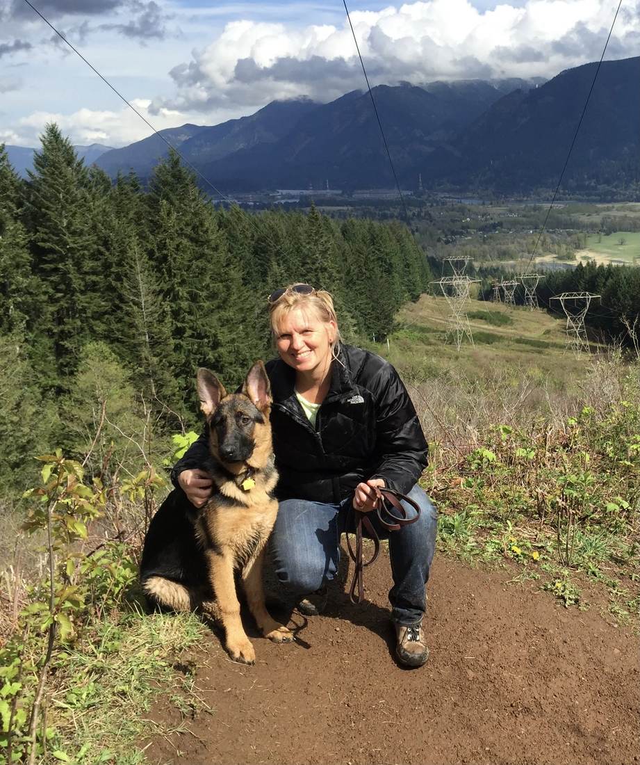 Robin kneeling on a mountain trail beside her German Shepherd, the valley behind them